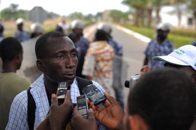 Journalist Ferdinand Ayite speaks to the press, as security forces try to prevent journalists and members of the public from protesting in front of the Palais des Congrès, in Lomé, Togo, 19 February 2013, Daniel Hayduk/AFP via Getty Images
